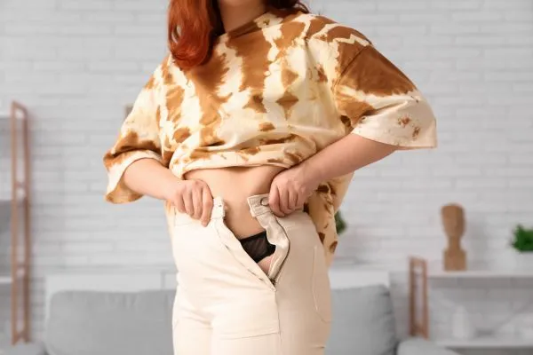 Image of woman trying to do her trousers up after pregnancy weight gain Woburn Sands