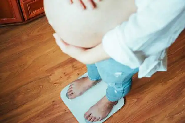 Image of woman weighing herself and experiencing weight gain through pregnancy Woburn Sands